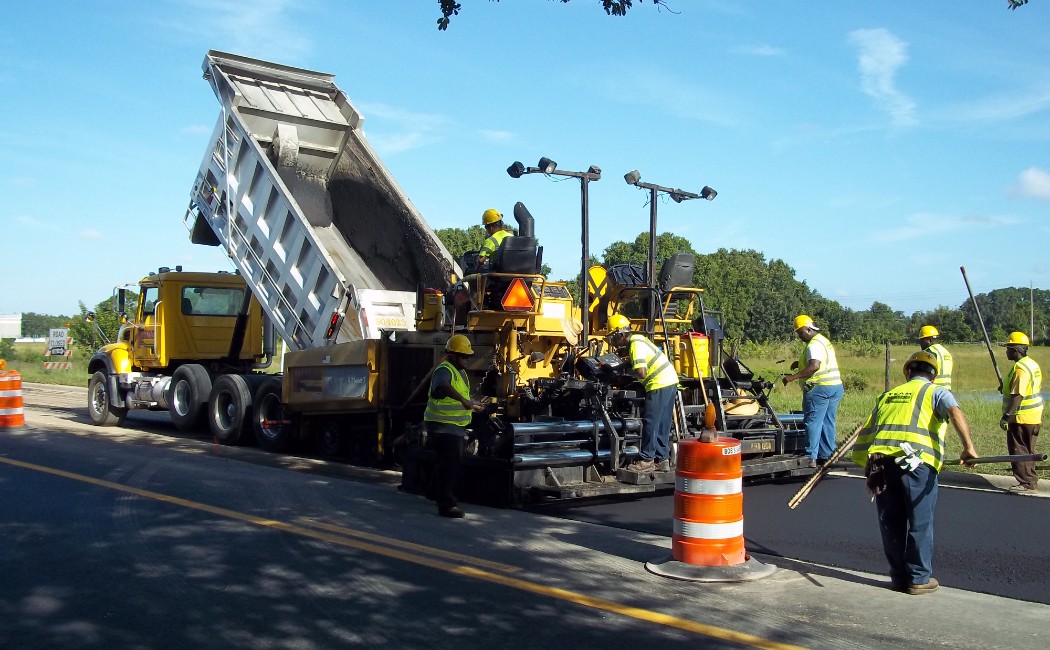 Workers performing asphalt work services using heavy machinery to lay fresh asphalt on a road for a smooth and durable pavement surface.