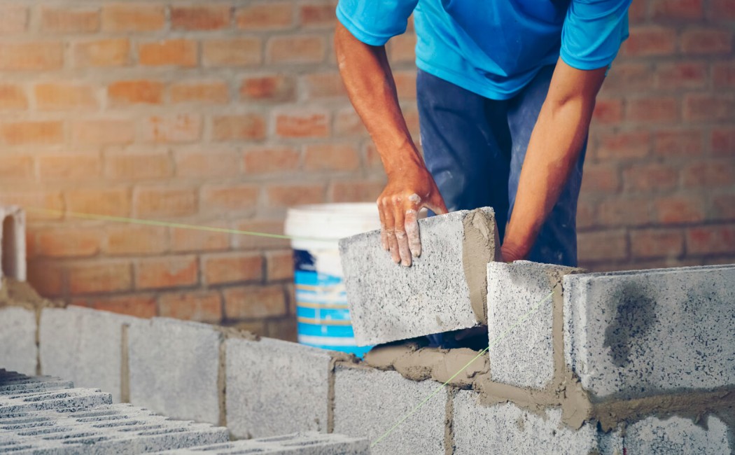 A construction worker carefully lays concrete blocks with mortar, demonstrating skilled craftsmanship in masonry services.