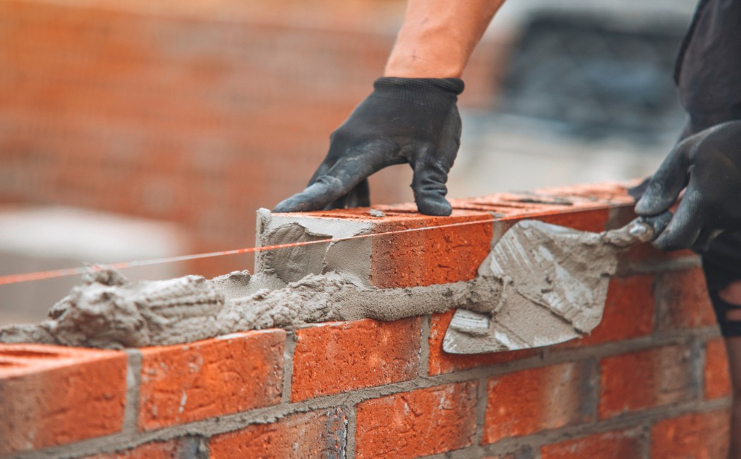 A construction worker precisely applies mortar and lays red bricks to build a strong wall, highlighting the expertise of a masonry work company.