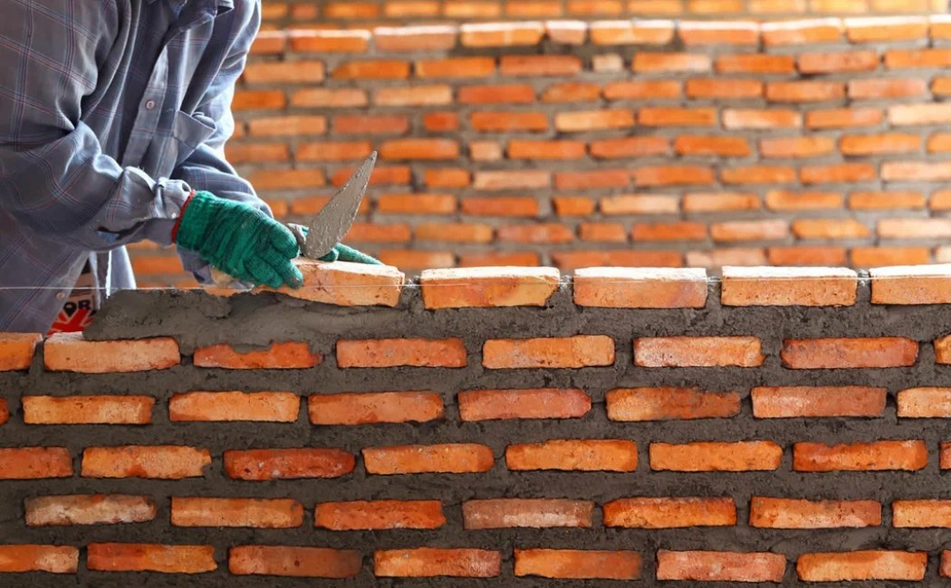 A worker skillfully laying bricks with mortar, showcasing the precision and craftsmanship of a masonry work company.