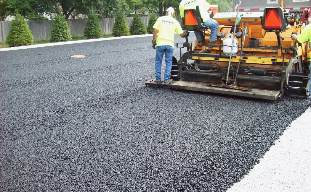 Workers performing asphalt work services using paving equipment to lay a fresh layer of asphalt, ensuring a smooth and durable road surface. 
