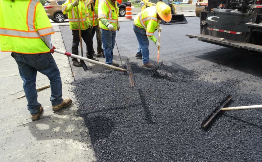 Workers performing asphalt paving services, spreading and leveling hot asphalt to create a smooth and even road surface.