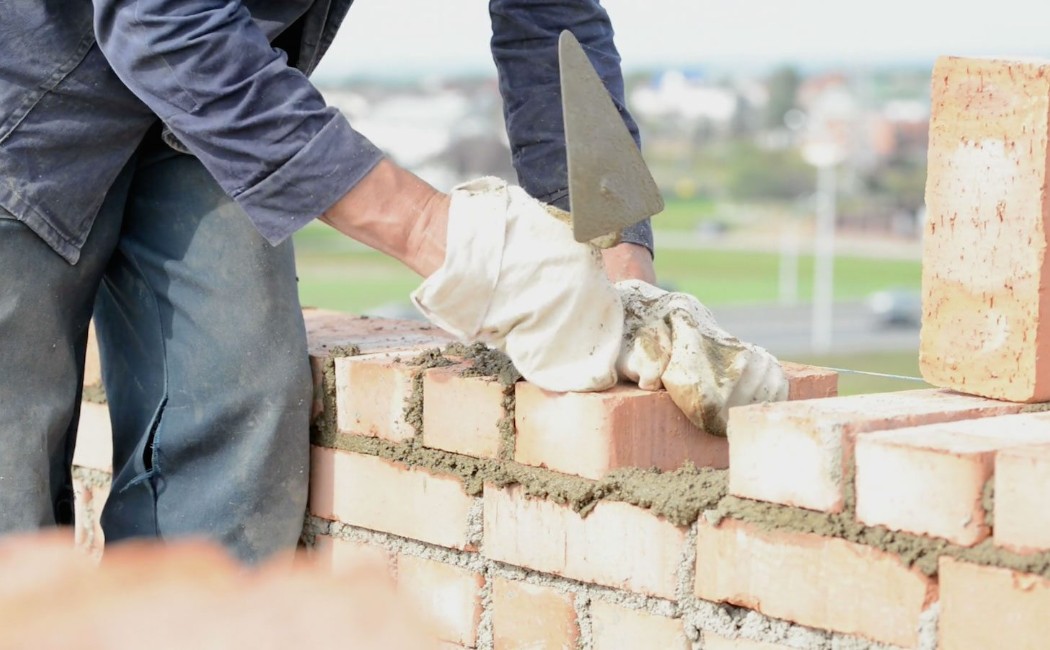 A skilled worker applies mortar and carefully lays bricks to build a sturdy wall, demonstrating expert craftsmanship by a masonry work company.