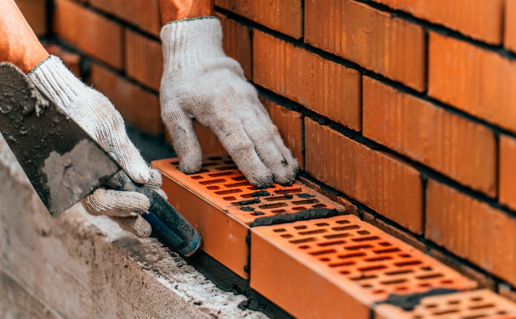 A mason carefully lays red bricks with precision and mortar, showcasing skilled craftsmanship by a professional masonry work company.